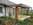Terrasse mit Holzkonstruktion überdacht, Schindelverkleidung im sichtbaren Flachdachbereich, 3 seitige Umbauung mit brauner Schiebeverglasung, eingelasseneen Belauchtung im großzügigem Dachüberstand aus Holz